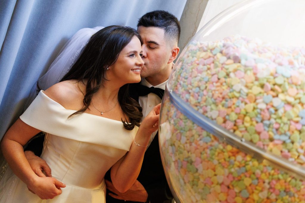 Groom kissing the bride's cheek beside a candy display at the reception