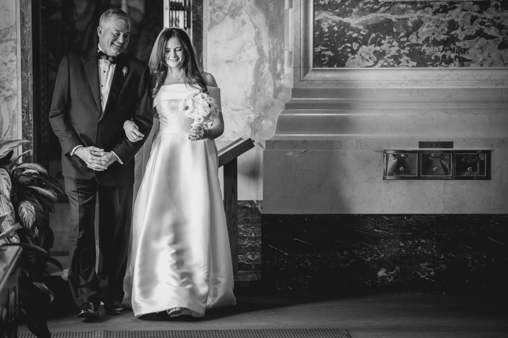Father walking the bride down the aisle inside a marble church, black and white photo