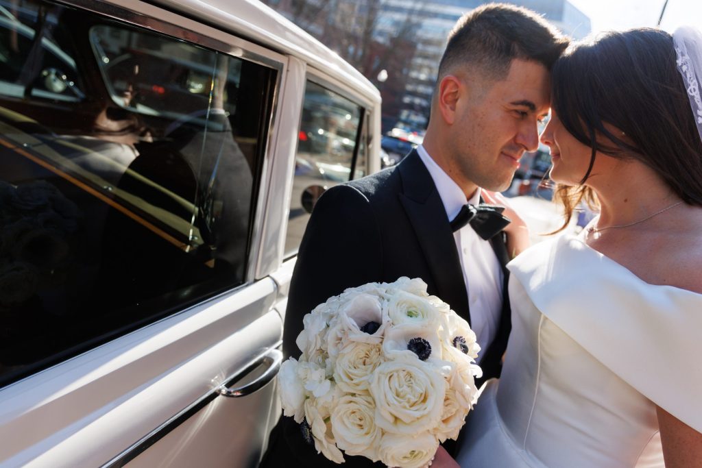 Bride and groom sharing a tender forehead-to-forehead moment beside their vintage car