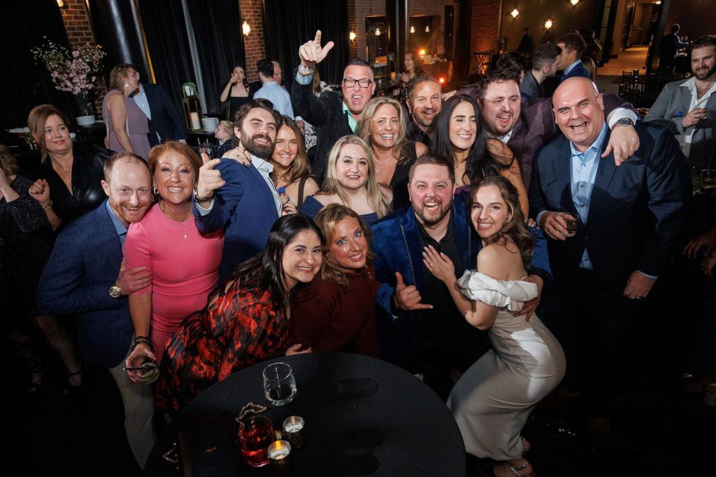 Large group of wedding guests smiling and celebrating together on the dance floor at the reception