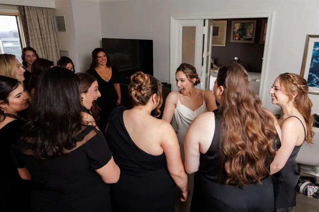 Bride surrounded by bridesmaids celebrating joyfully in a circle while getting ready